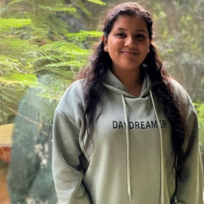 Physiotherapy student, Shali Thevarasan standing in front of a window overlooking trees. Supplied.